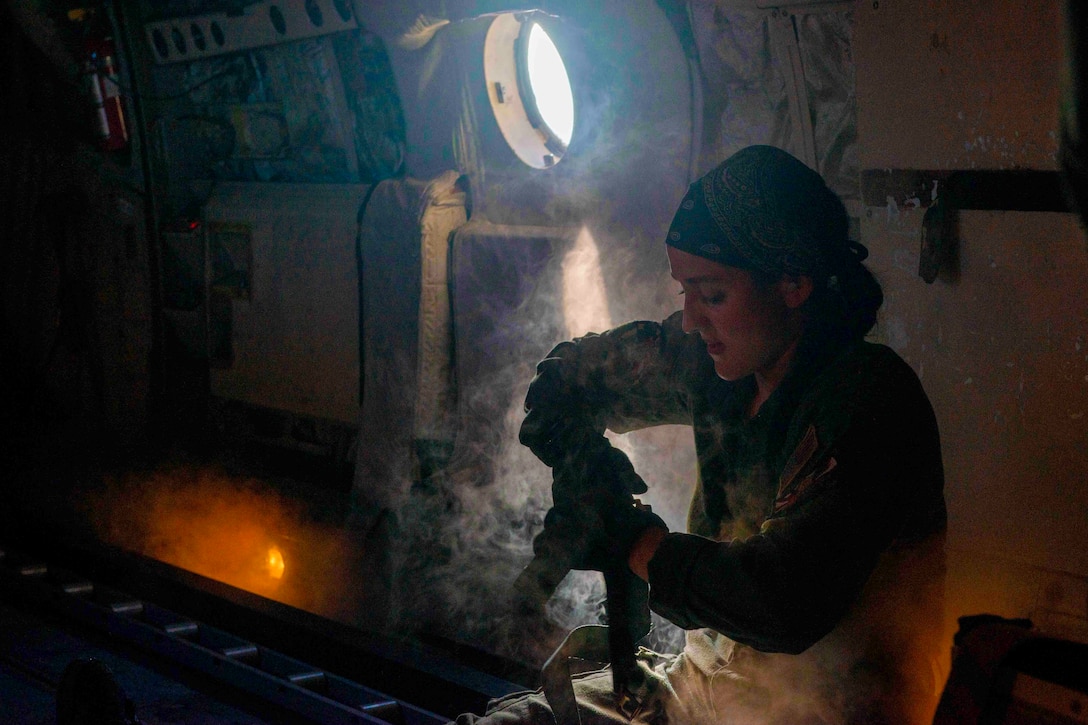 A sailor moves gear in a dark room.