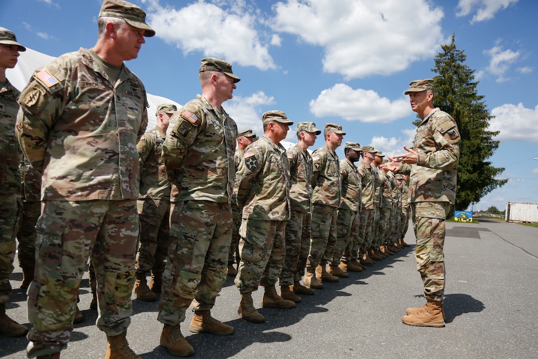 A soldier talks to a formation of troops standing at parade rest.