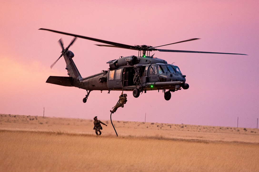 Airmen use a rope to deploy from a helicopter.