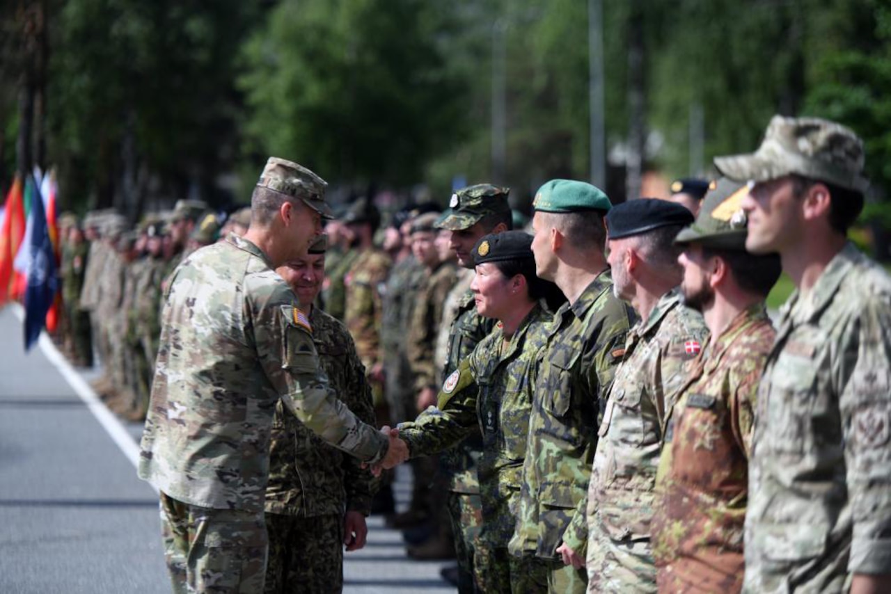 A uniformed service member shakes the hand of another uniformed service member who is standing in a line of various domestic and foreign military members.