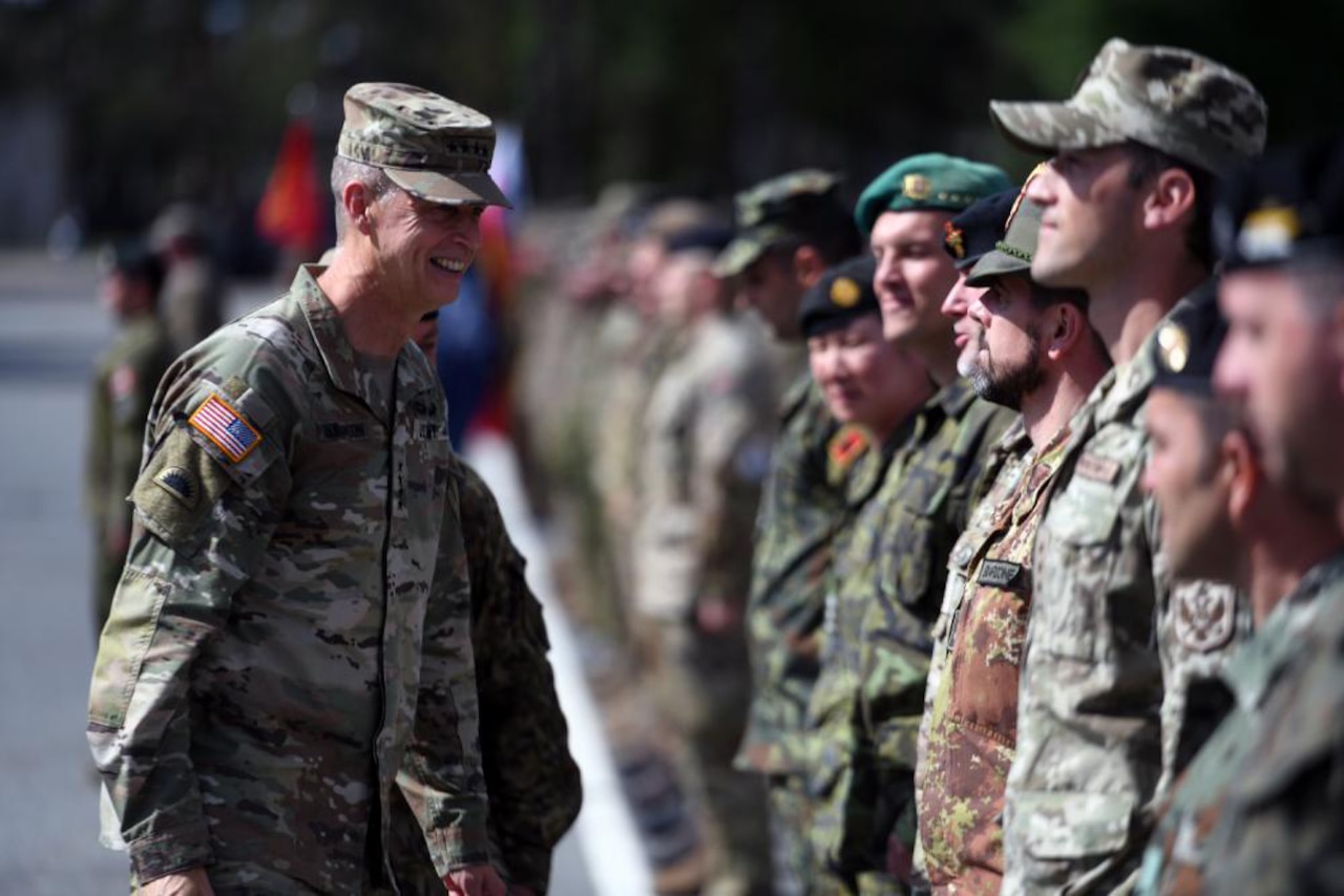 A uniformed service member smiles at another uniformed service member who is standing in a line of various domestic and foreign military members.