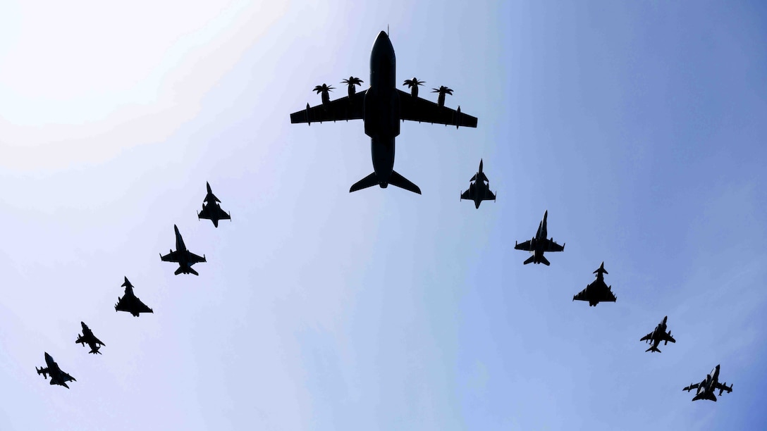 Eleven aircraft of different shapes fly in a V formation in blue sky.