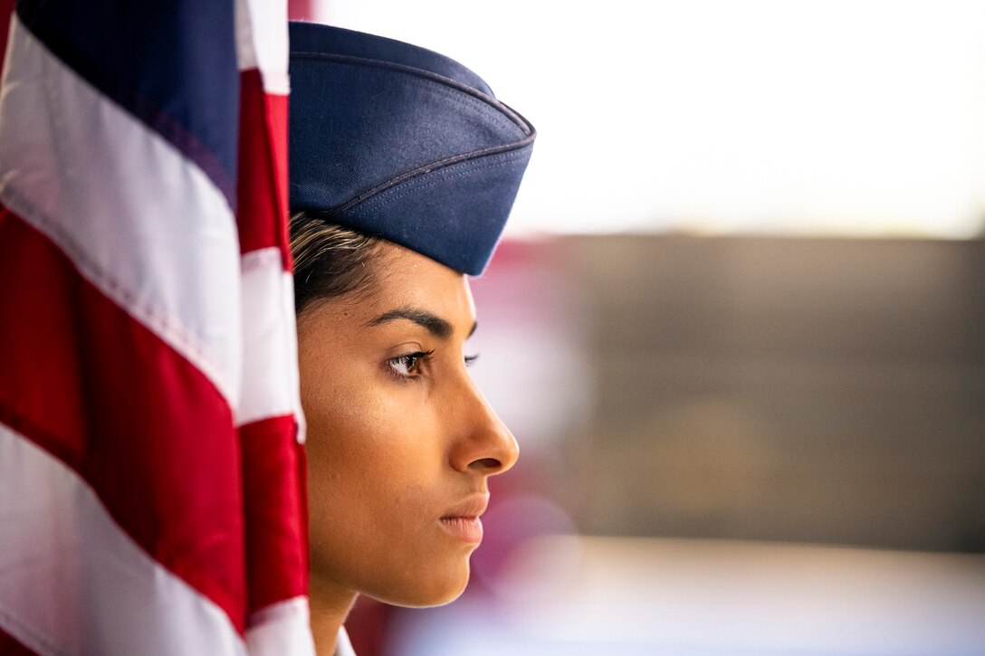 An airman stands at attention while holding an American flag.