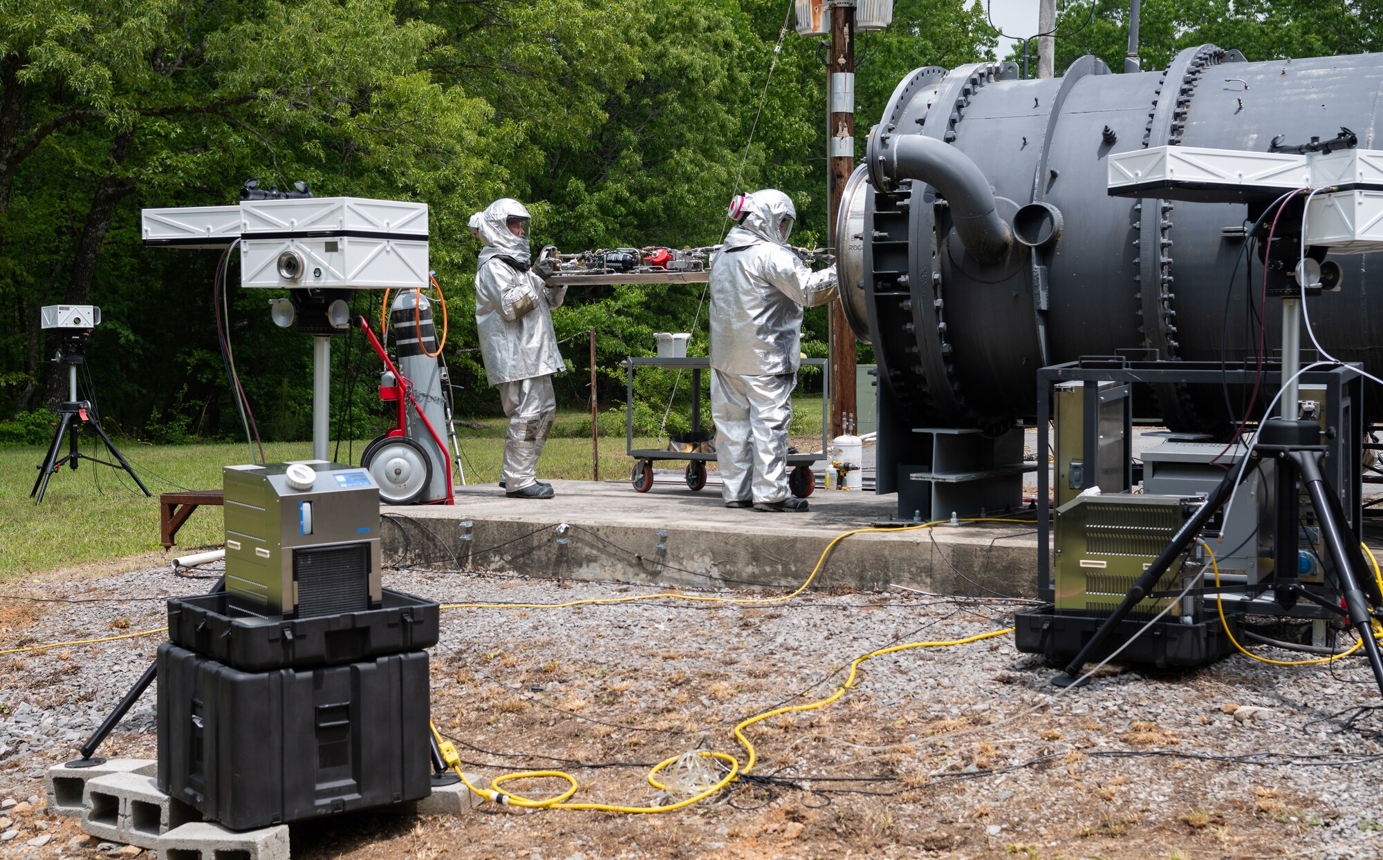 Two men in protective suits working remove a towed airborne plume simulator fuel tank