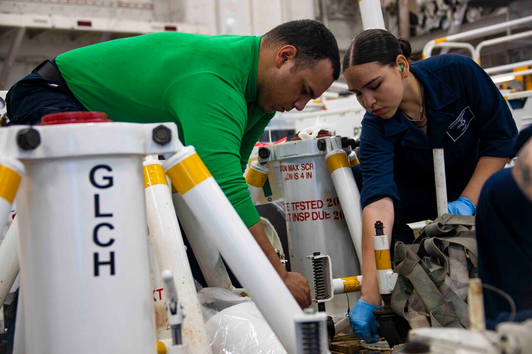 Two sailors work on equipment.