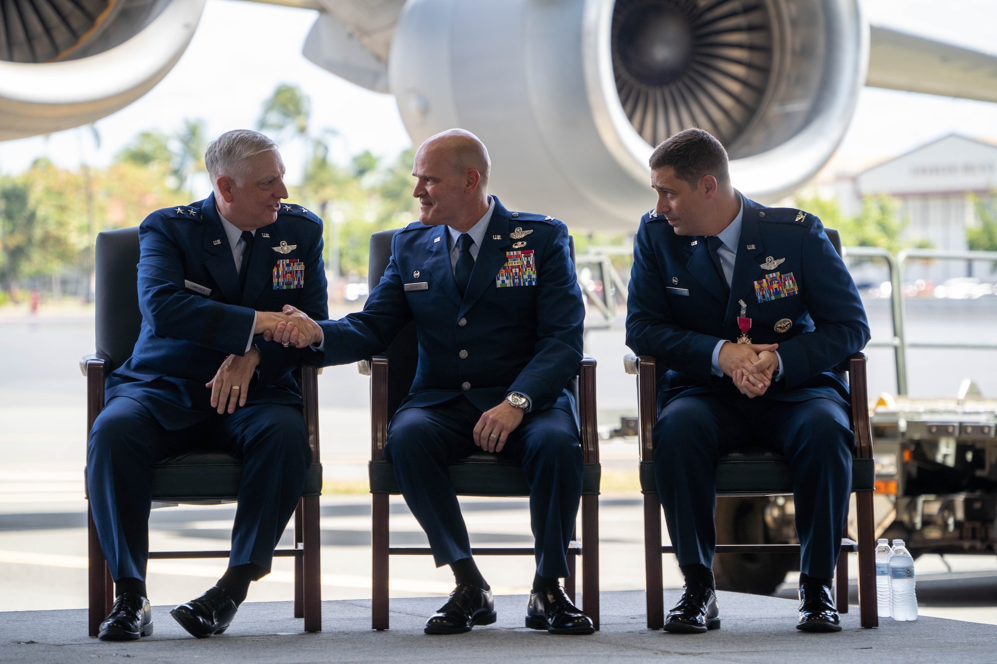 U.S. Air Force Maj. Gen. Mark D. Camerer, left, U.S. Air Force Expeditionary Center commander, shakes hands with Col. Kyle A. Benwitz, 515th Air Mobility Operations Wing commander, while joined on stage by Col. Dan Cooley, former 515th AMOW commander, during a change of command ceremony June 28, 2022.