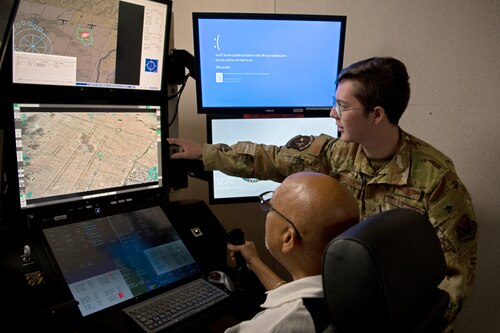 U.S. Air Force Senior Airman Caspar, 482nd Attack Squadron MQ-9 Reaper sensor operator, right, directs Jim McCain, 20th Operations Group honorary commander, in a simulator during an immersion tour at Shaw Air Force Base, S.C., June 22, 2022. Operating the simulator gives guests an opportunity to experience firsthand what MQ-9 crews do every day. (U.S. Air Force photo by Staff Sgt. Kelsey Owen)