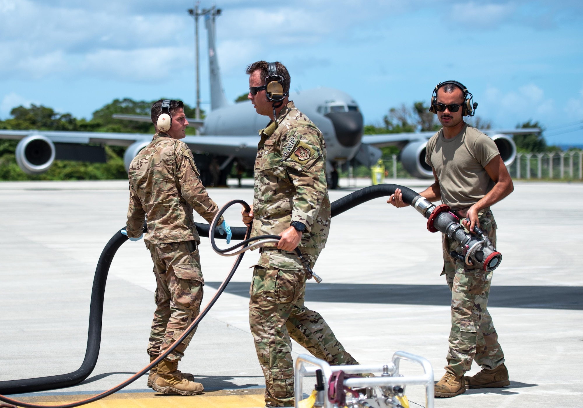 Airmen hold a fuel hose while performing hot-pit refueling