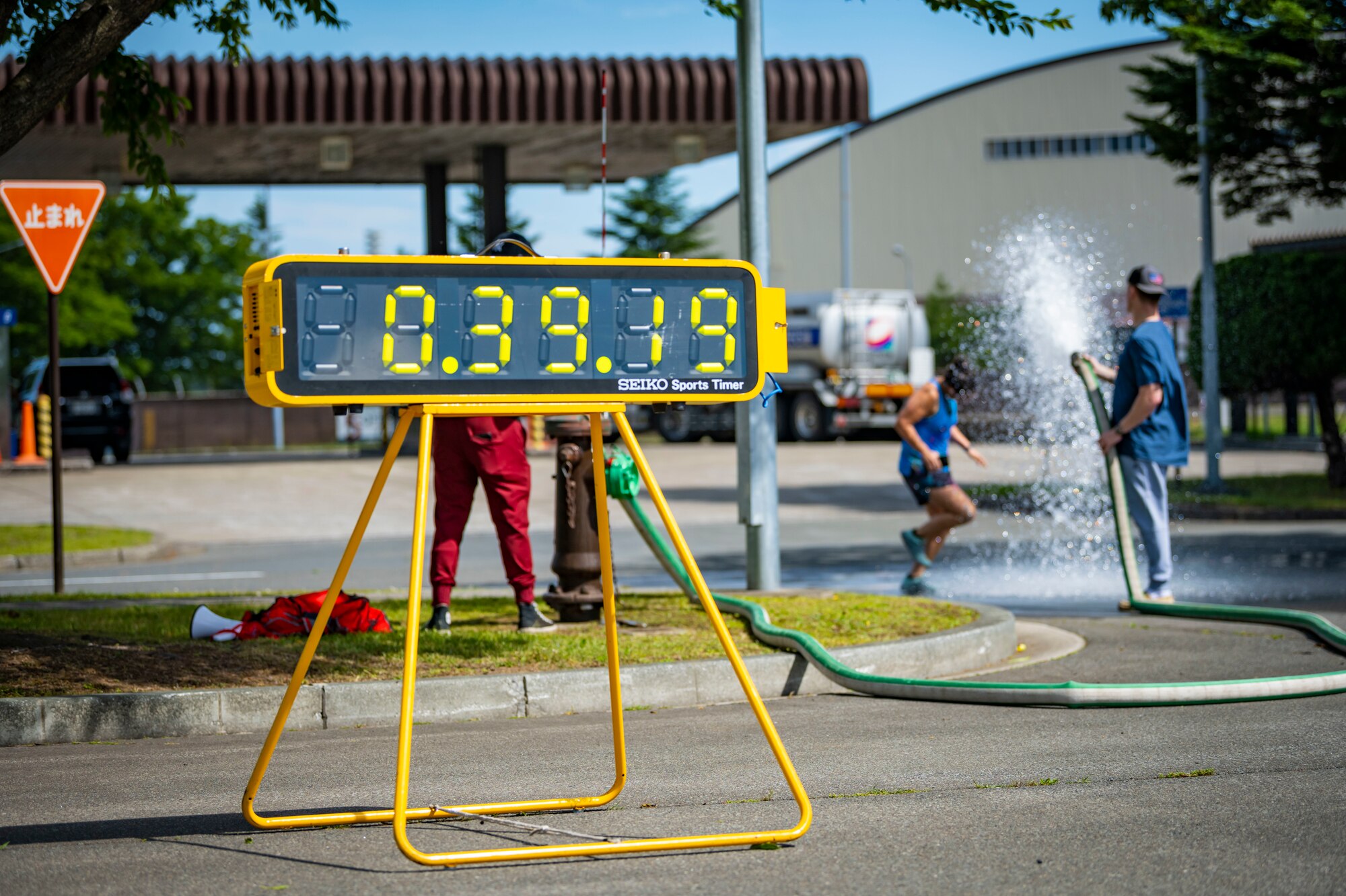 A yellow stop watch keeps track of time while runners cross the finish line in the background.