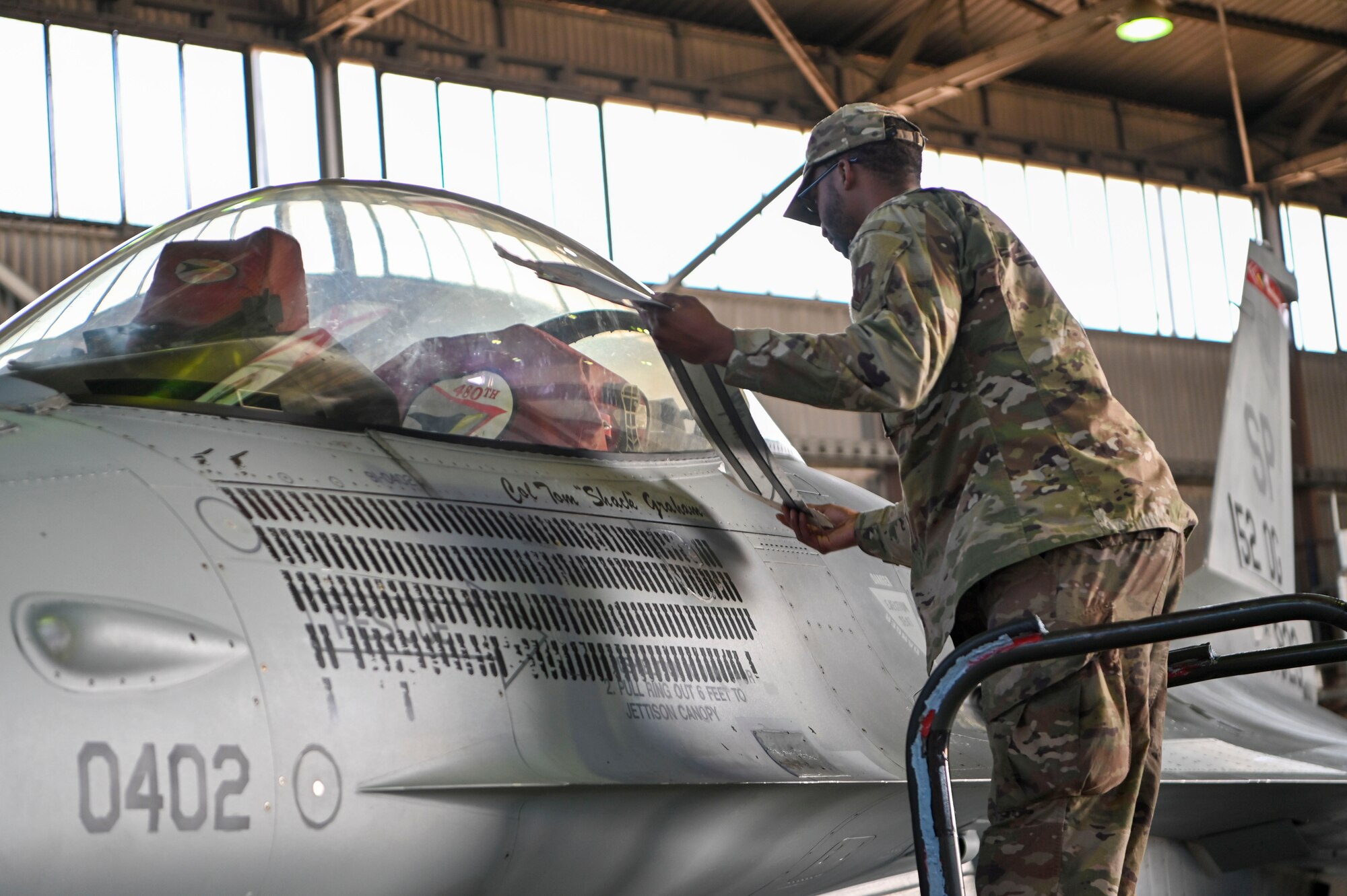 Staff Sgt. John Reid, 52nd Aircraft Maintenance Squadron crew chief, unveils the name of Col. Thomas Graham, 52nd Operations Group commander, on the 52nd OG F-16 Viper flagship, during an assumption of command ceremony, June 28, 2022, on Spangdahlem Air Base, Germany. It is an Air Force tradition to rename a commander’s flagship and have their name painted on the aircraft, depicting it as the group commander’s. (U.S. Air Force photo by Senior Airman Jessica Sanchez-Chen)