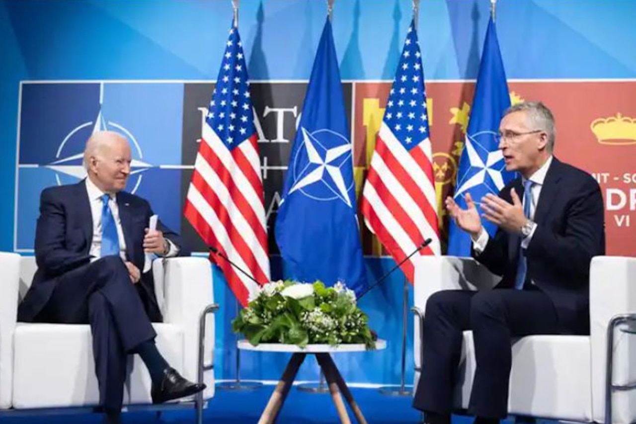 Two men sit in chairs and speak to each other.