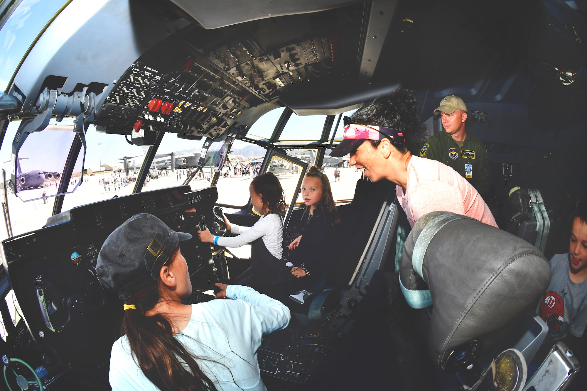 Three girls sit in the cockpit of an aircraft while their Kristen Middlestead and Maj. Livingston look on from behind the seats.