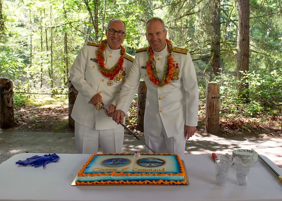 Rear Adm. Robert Gaucher and Rear Adm. Mark Behning cut a ceremonial cake following a change of command ceremony onboard Naval Base Kitsap – Bangor, Wash., June 28, 2022.