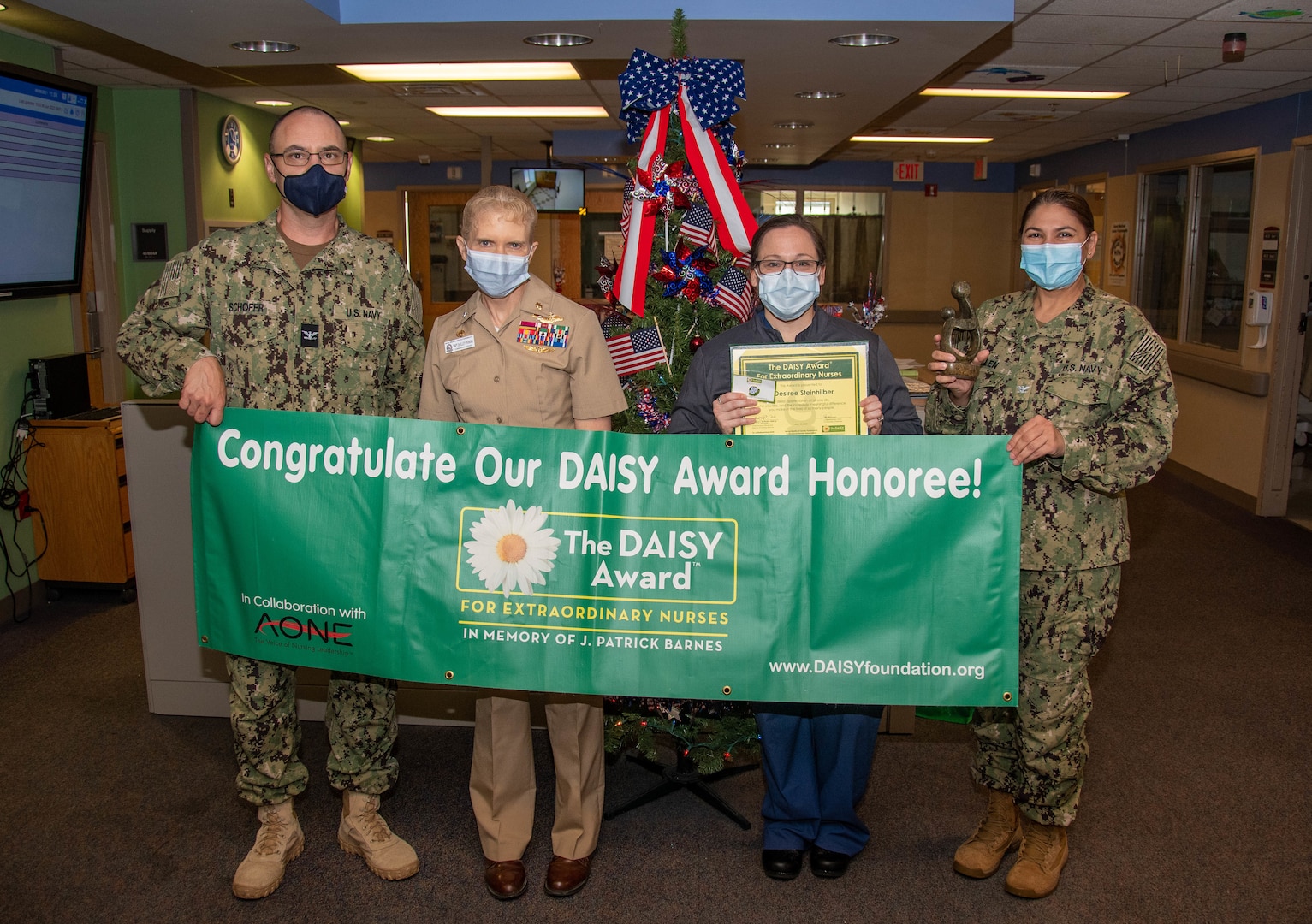 PORTSMOUTH, Va. (June 6, 2022) - Capt. Shelley Perkins, commanding officer of Naval Medical Center Portsmouth (NMCP), center left, and Capt. Joel Schofer, executive officer of NMCP, left, present Lt. Desiree Steinhilber, an NMCP nurse, with a DAISY Award during a ceremony, June 6. The DAISY Award was established by The DAISY Foundation in 1999 by the family of J. Patrick (Pat) Barnes, a patient who lost his life to the auto-immune disease ITP. Barnes’ family wanted to recognize the incredible care that the nurses provided him before his death and created the award now embraced by healthcare organizations around the world. (U.S. Navy photo by Mass Communication Specialist 2nd Class Dylan M. Kinee/Released)