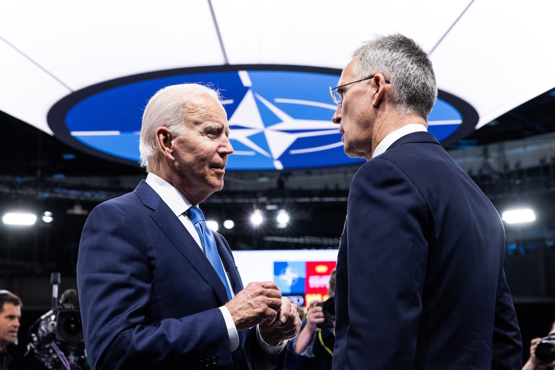 Two men in business attire converse in front of news media.