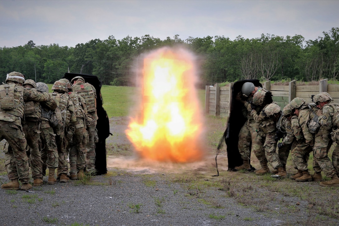 Soldiers stand in two lines behind a shield near an explosive during training.