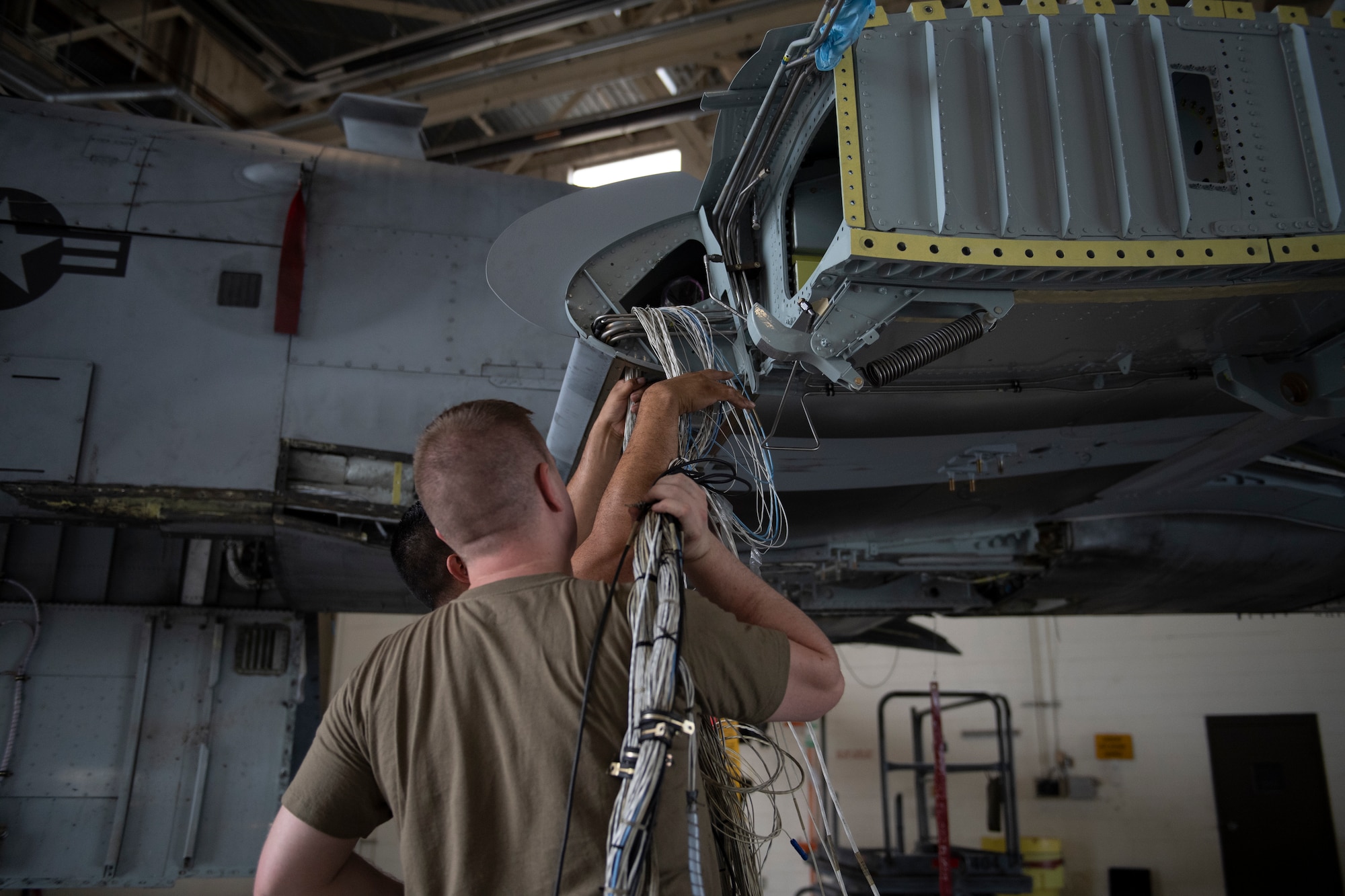 U.S. Air Force Tech. Sgt. Abelino Ledesma and Staff Sgt. Jared Jackson, 309th Aircraft Maintenance Group electrical and environmental craftsmen, insert electrical wires into an A-10C Thunderbolt II wing at Moody Air Force Base, Georgia, June 21, 2022. The 309th AMXG arrived from Hill Air Force Base, Utah, to remove and replace the wings on an A-10C. The wires from the old wing were taken out, recycled and configured together to fit into the new wing. (U.S. Air Force photo by Airman 1st Class Rachel Coates)