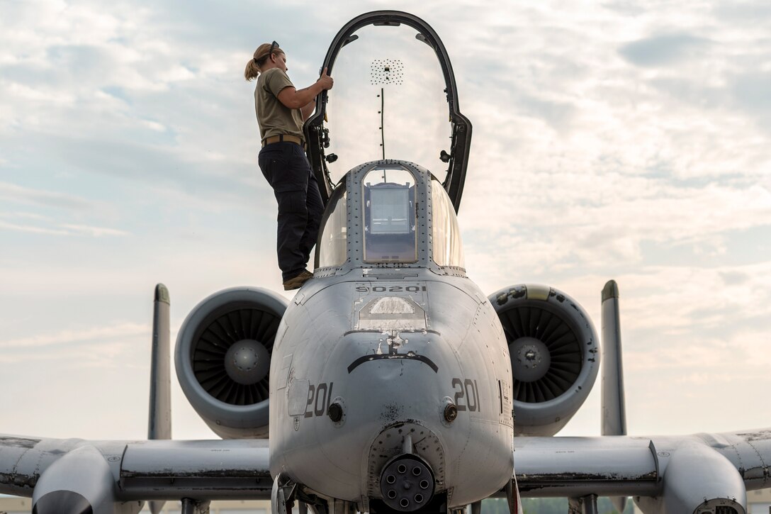An airman stands on an aircraft and opens the canopy.