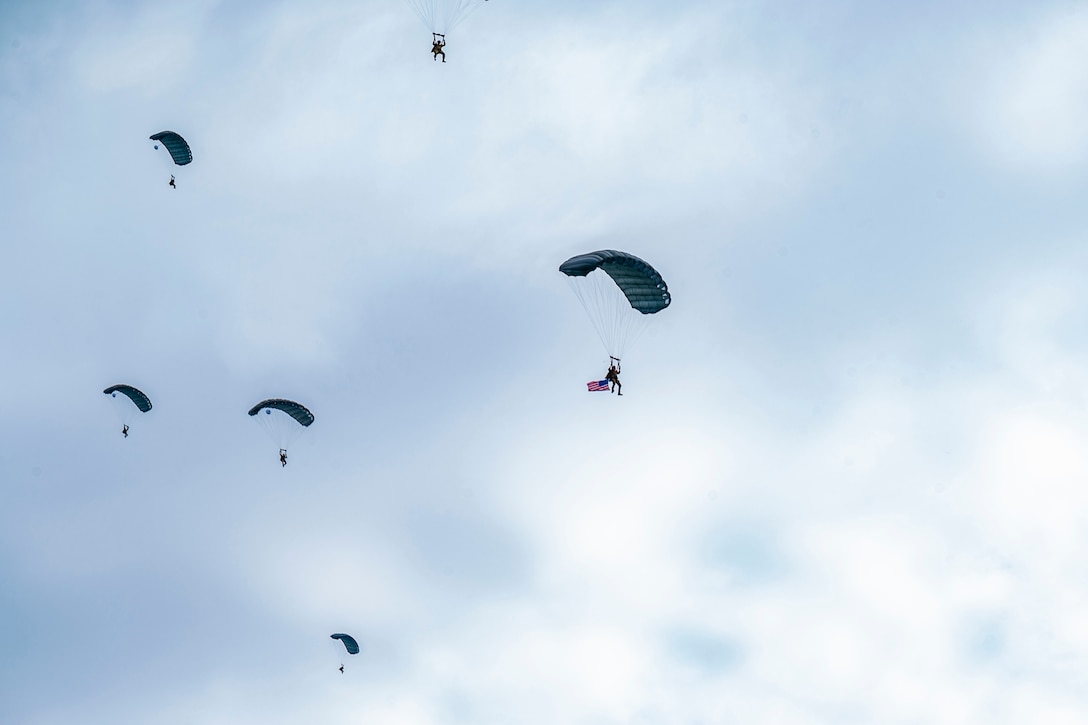 Soldiers parachute in a blue sky.