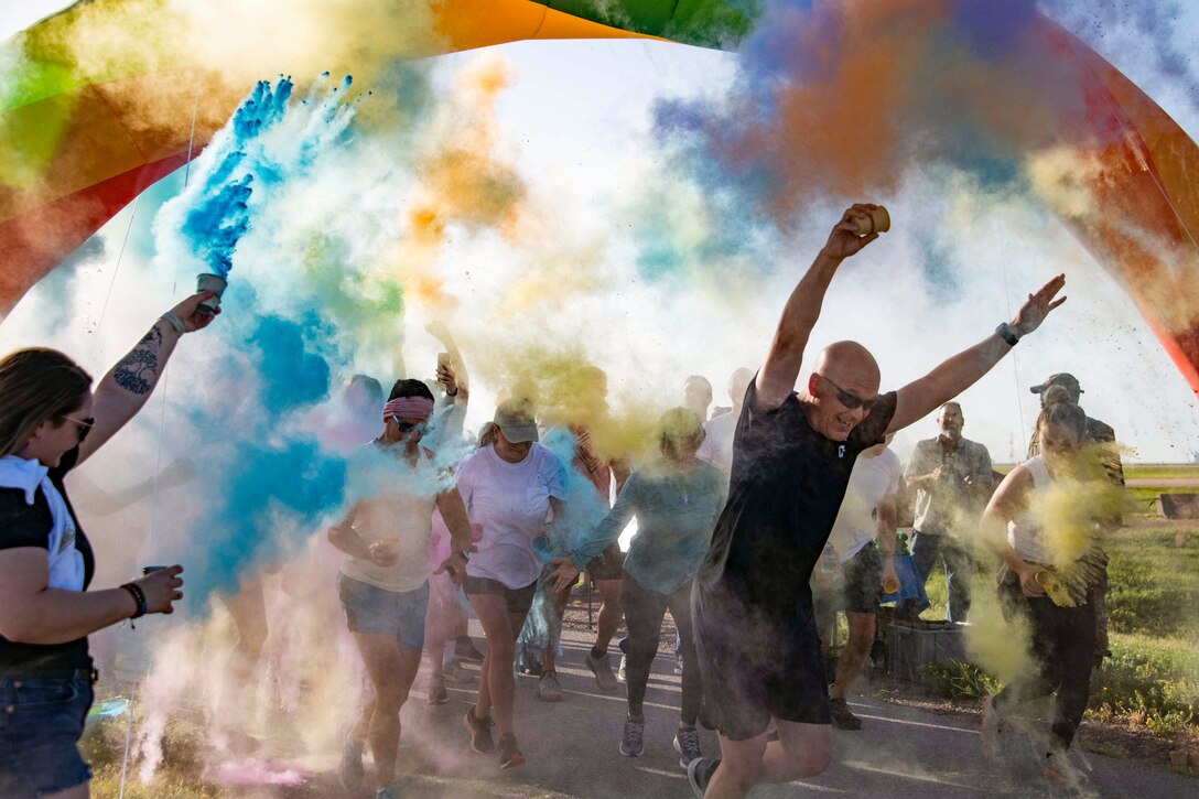 Spectators throw colored powder on runners passing through a multicolored arch.