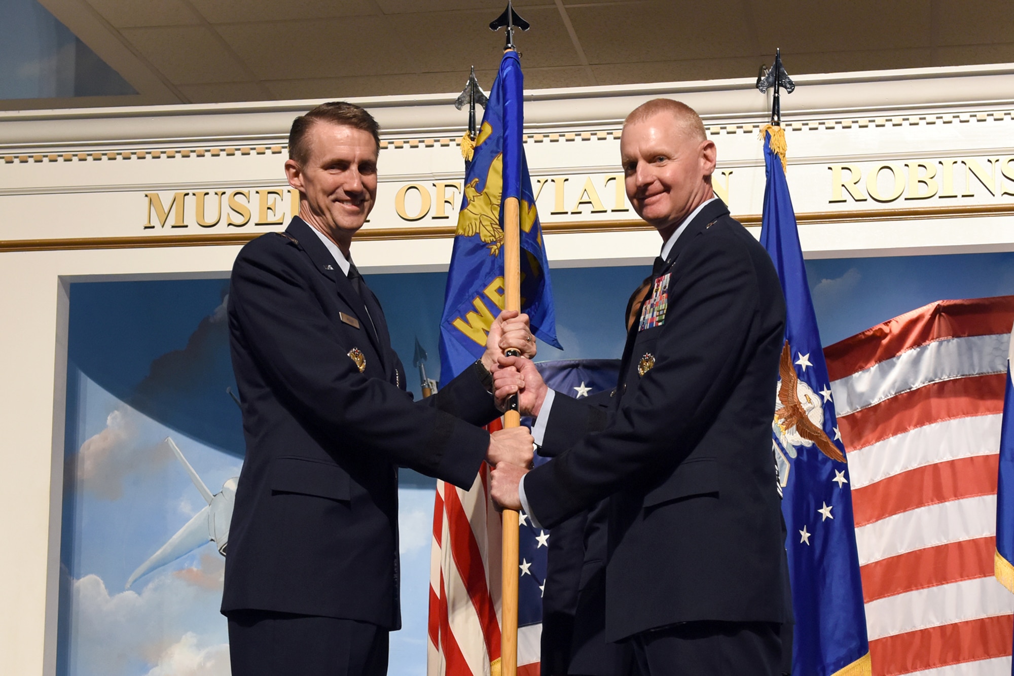Photo shows two men holding a flag between them.