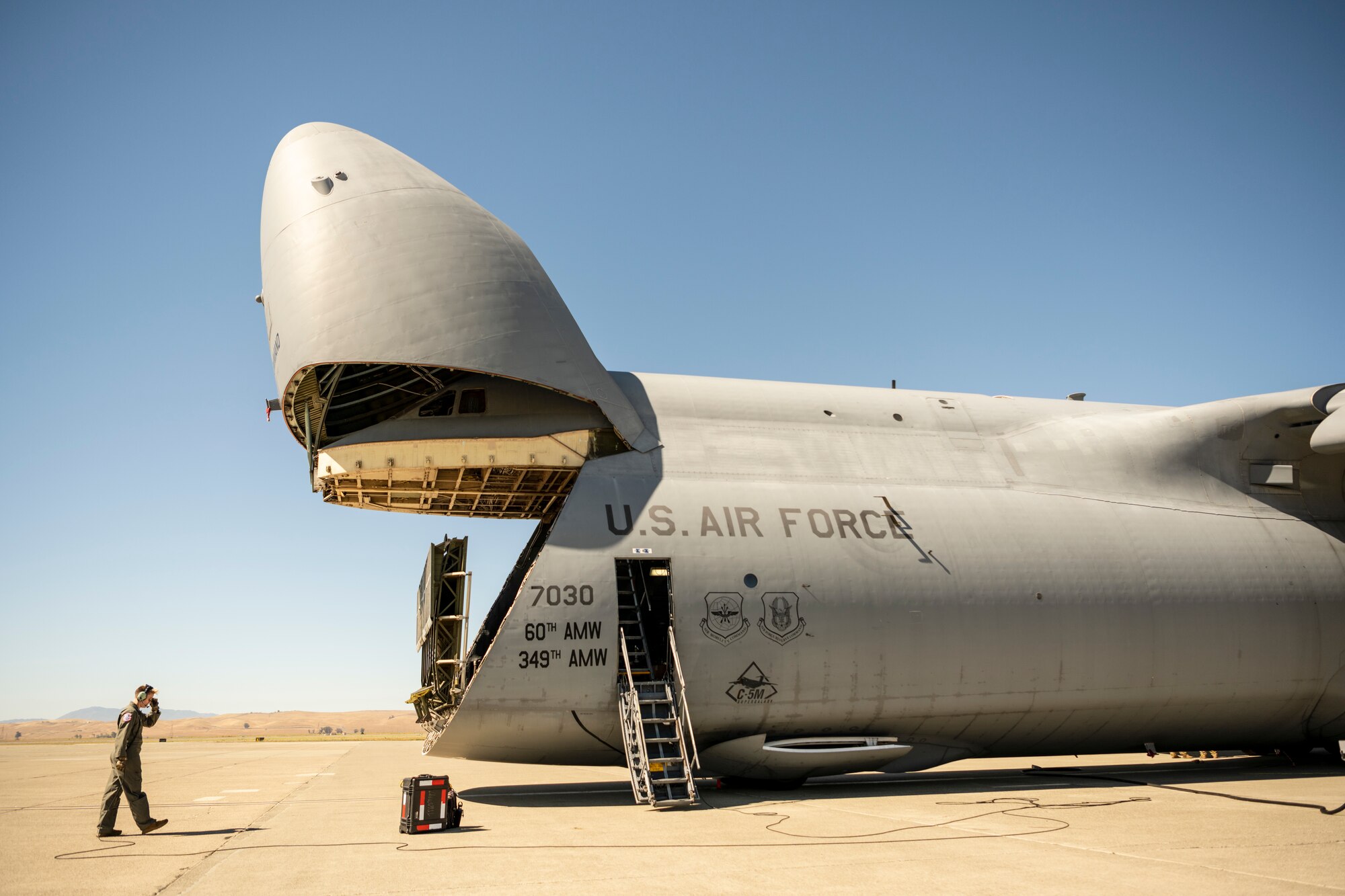 A woman in a flight suit watches a large door open in front of a large military airplane.