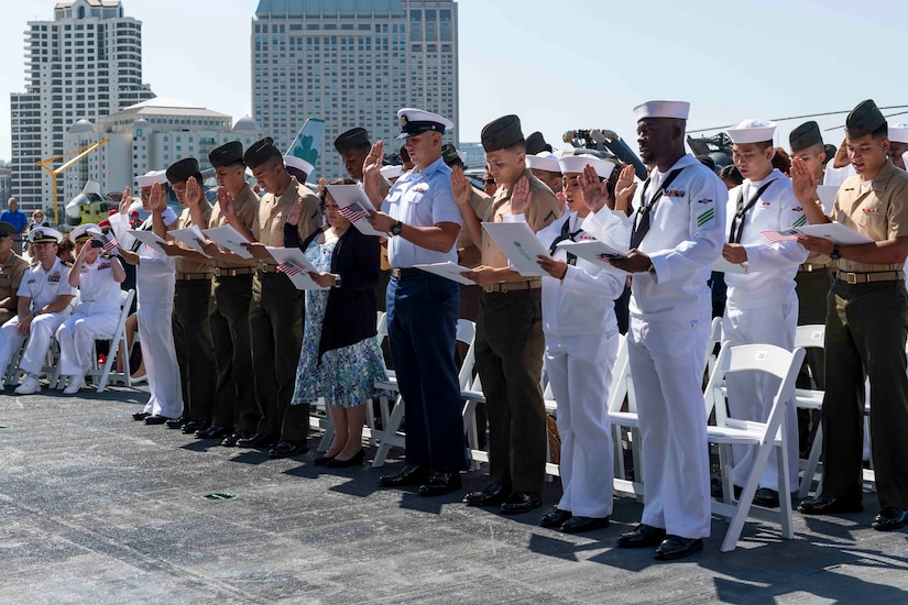 A group of service members in uniform stand and raise their right hand as they read from a document held in their other hand.