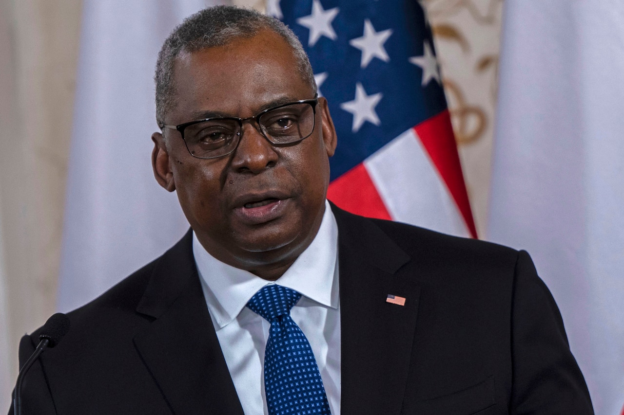 Secretary of Defense Lloyd J. Austin III speaks in a room in front of an American flag.