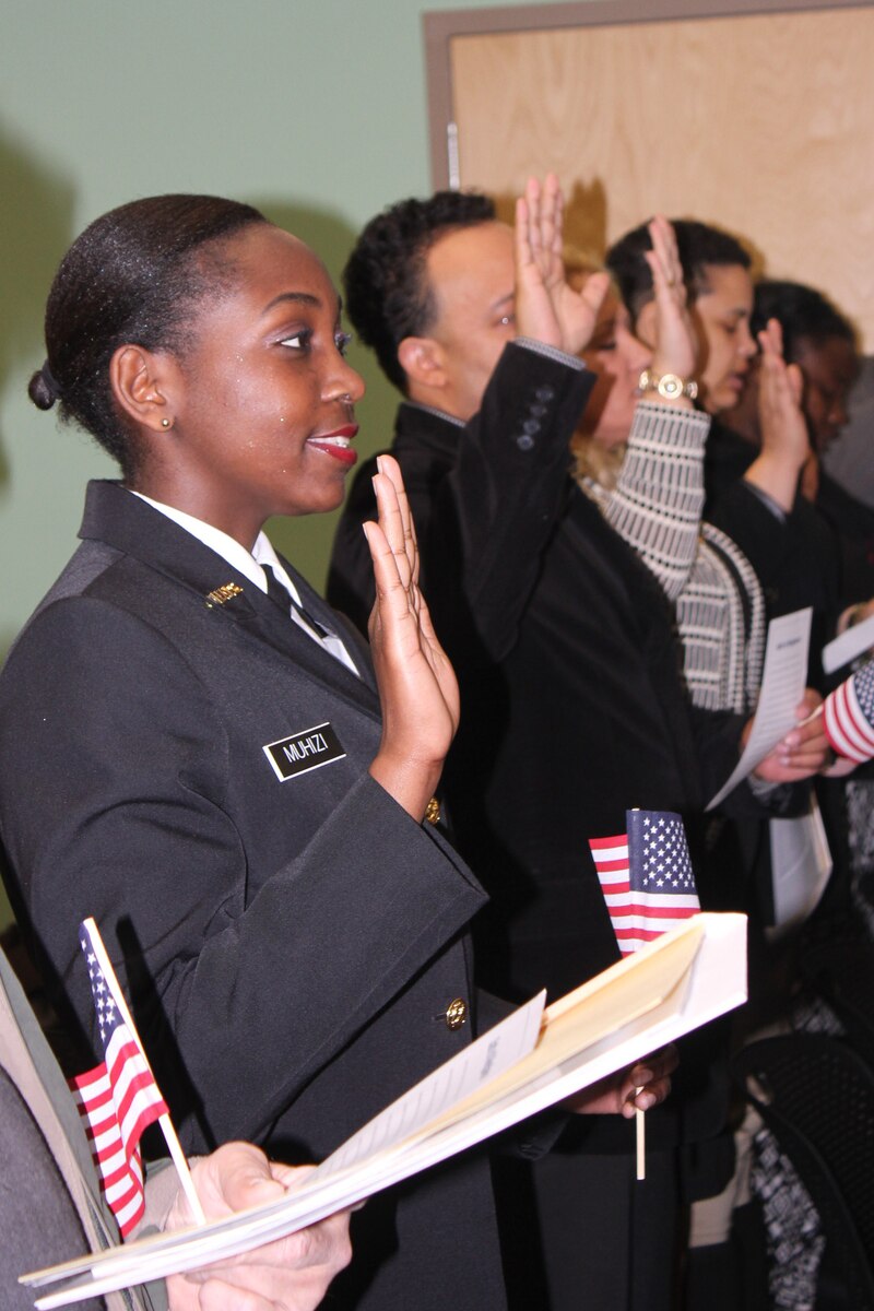 A woman in a formal dress uniform stands and raises her right hand together with a line of people.