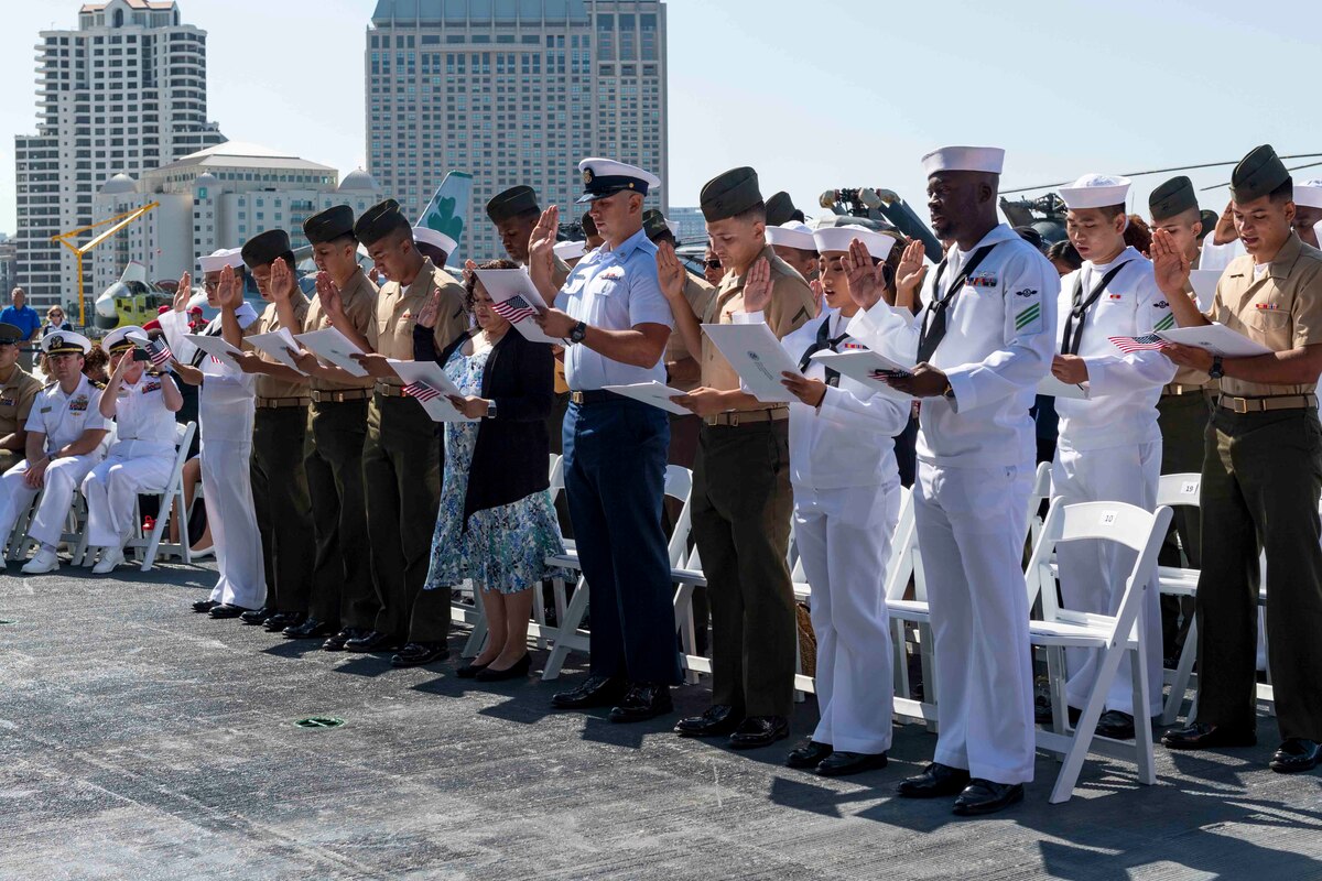 A group of service members in uniform stand and raise their right hand as they read from a document held in their other hand.
