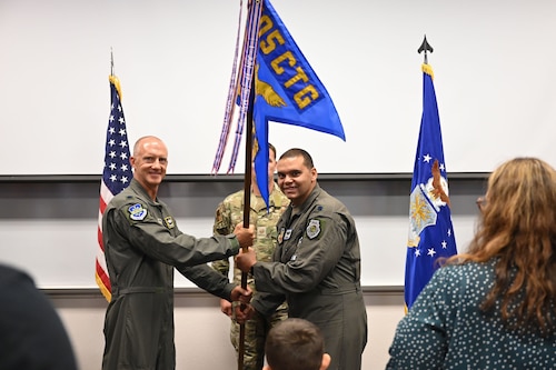 photo of two USAF Airmen holding unit guidon flag between them with USAF Airmen standing behind them