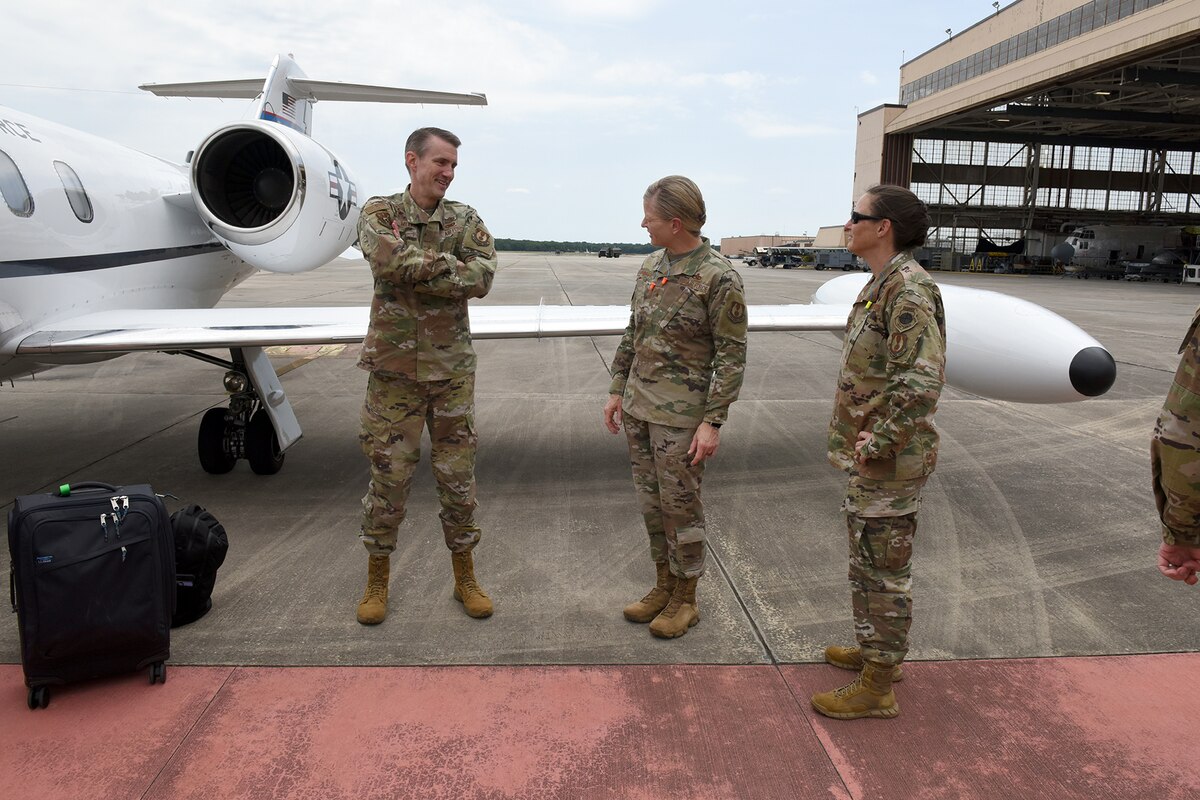 Photo shows three people standing on flight line next to small plane.