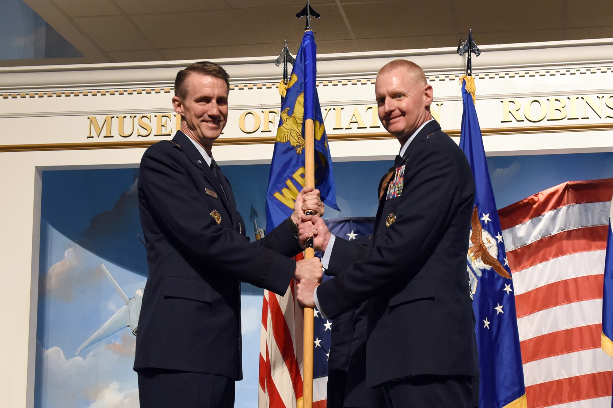 Photo shows two men holding a flag between them.