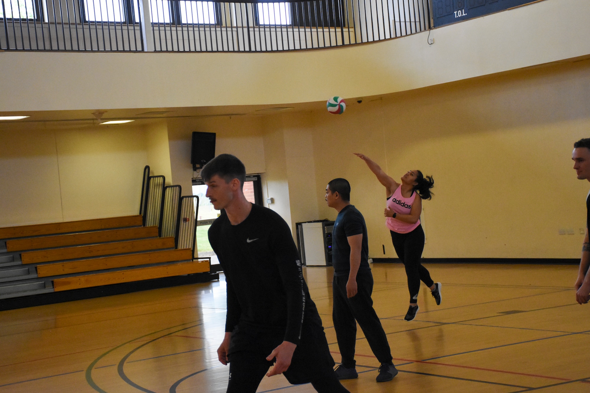 A woman in a pink shirt serves a volleyball while her teammates wait for the return.