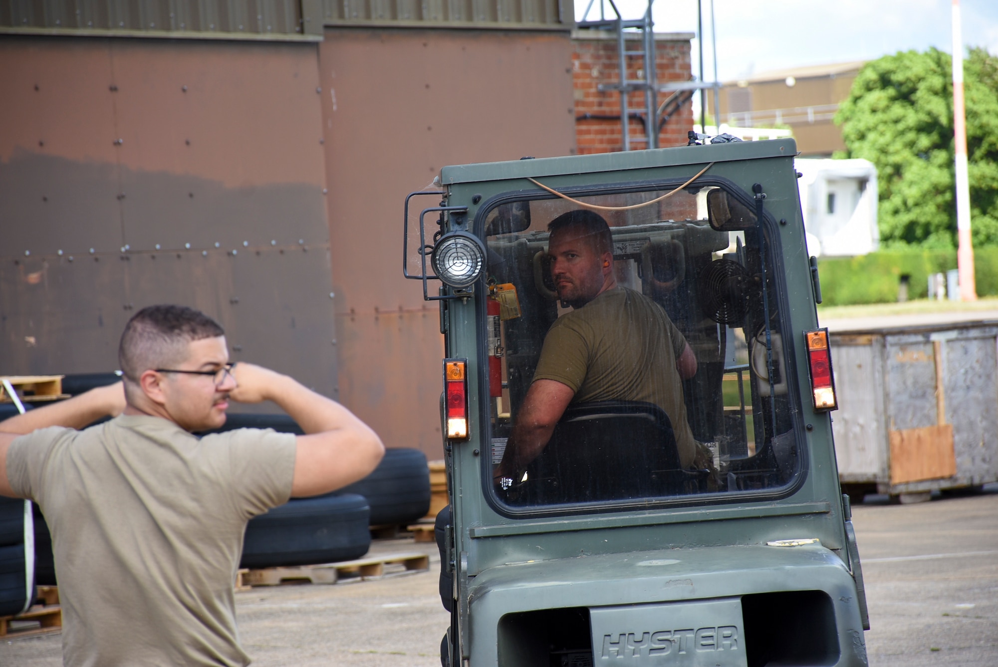 A man motions with his arms to direct a forklift driver as he is backing up.