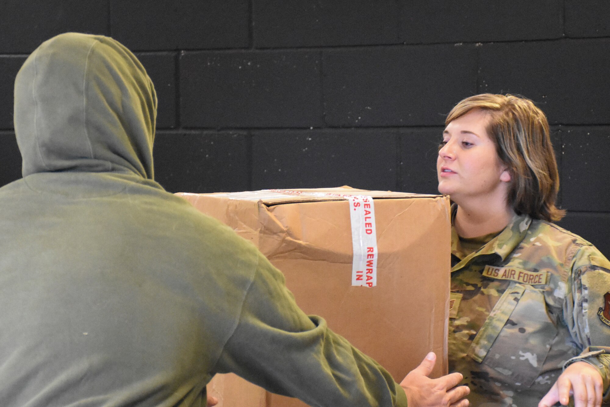 A woman hands a package to man in a greed hooded sweatshirt at a postal counter.