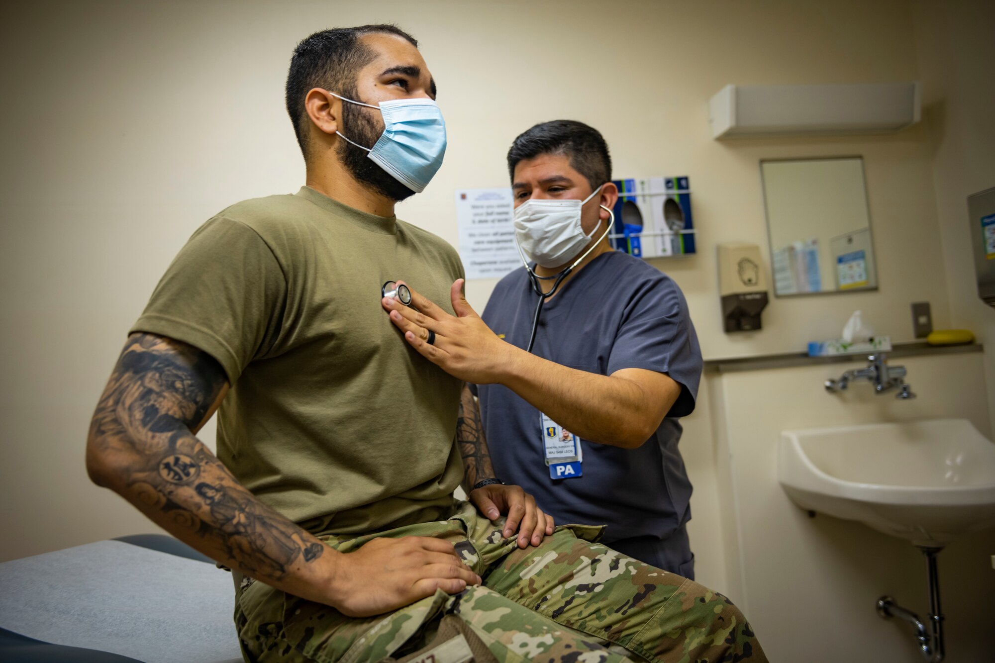 Military member in scrubs checks the heart rate of a military member in uniform