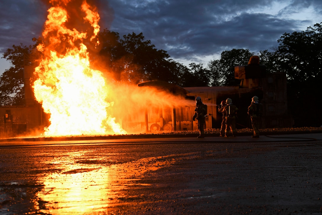 Several firefighters use a hose to put out a large blaze at night.