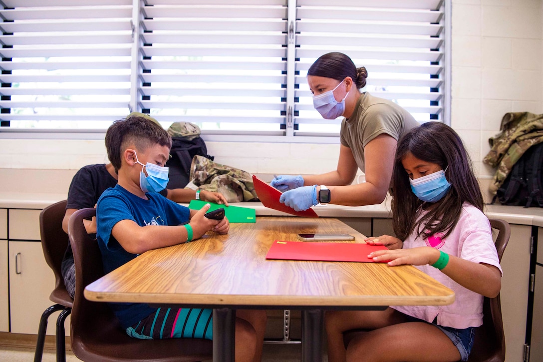 An airman works with children at a table.