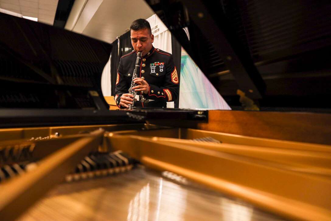 A Marine plays the clarinet in front of a piano.