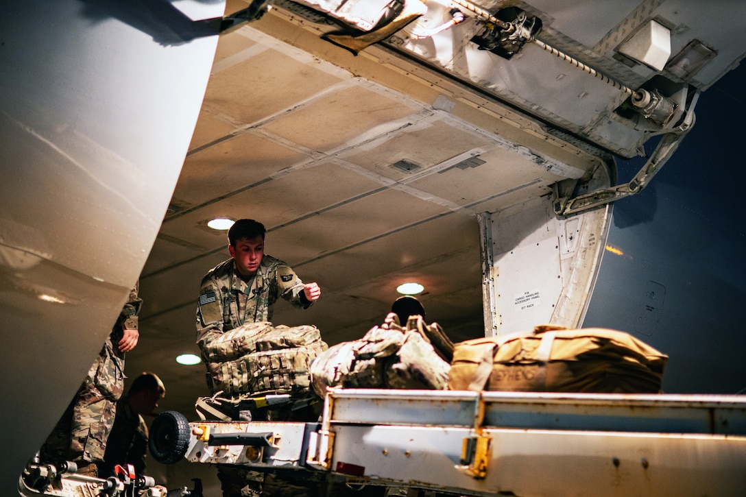 A soldier places bags and packs on a ramp leading out of an aircraft.