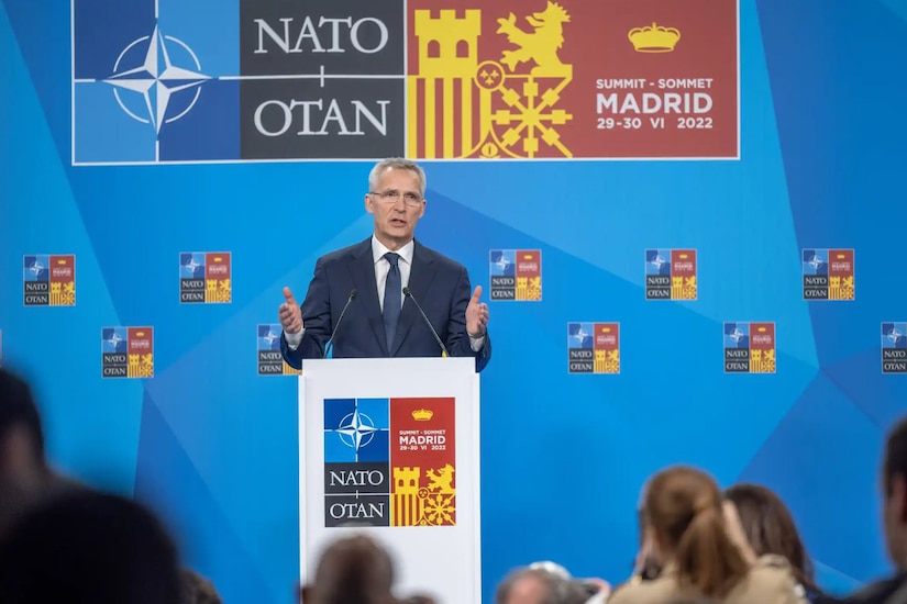 A man dressed in a business suit stands at a lectern and speaks to an audience.