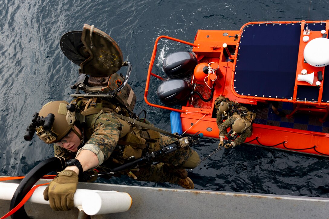 Marines climb from a small boat onto a ship at sea.