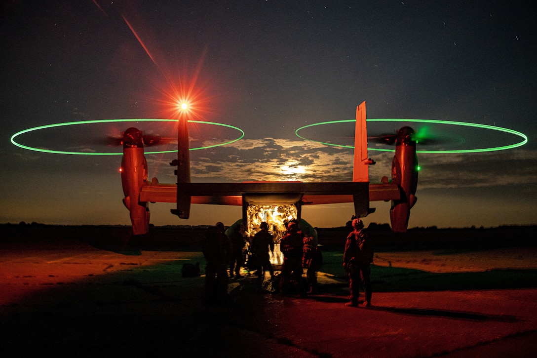 Marines and sailors board a CV-22 Osprey at night.