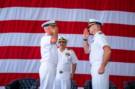 Naval Officers salute each other in front of the American Flag