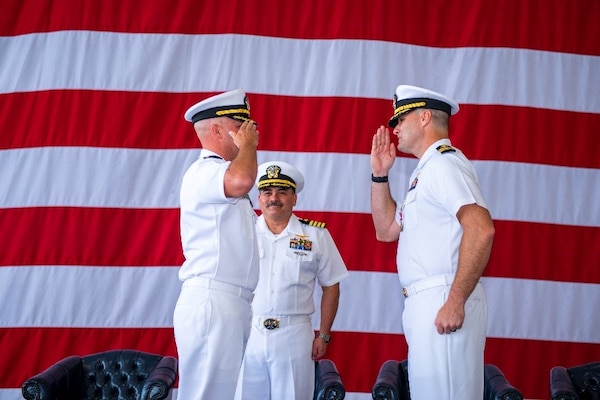 Naval Officers salute each other in front of the American Flag