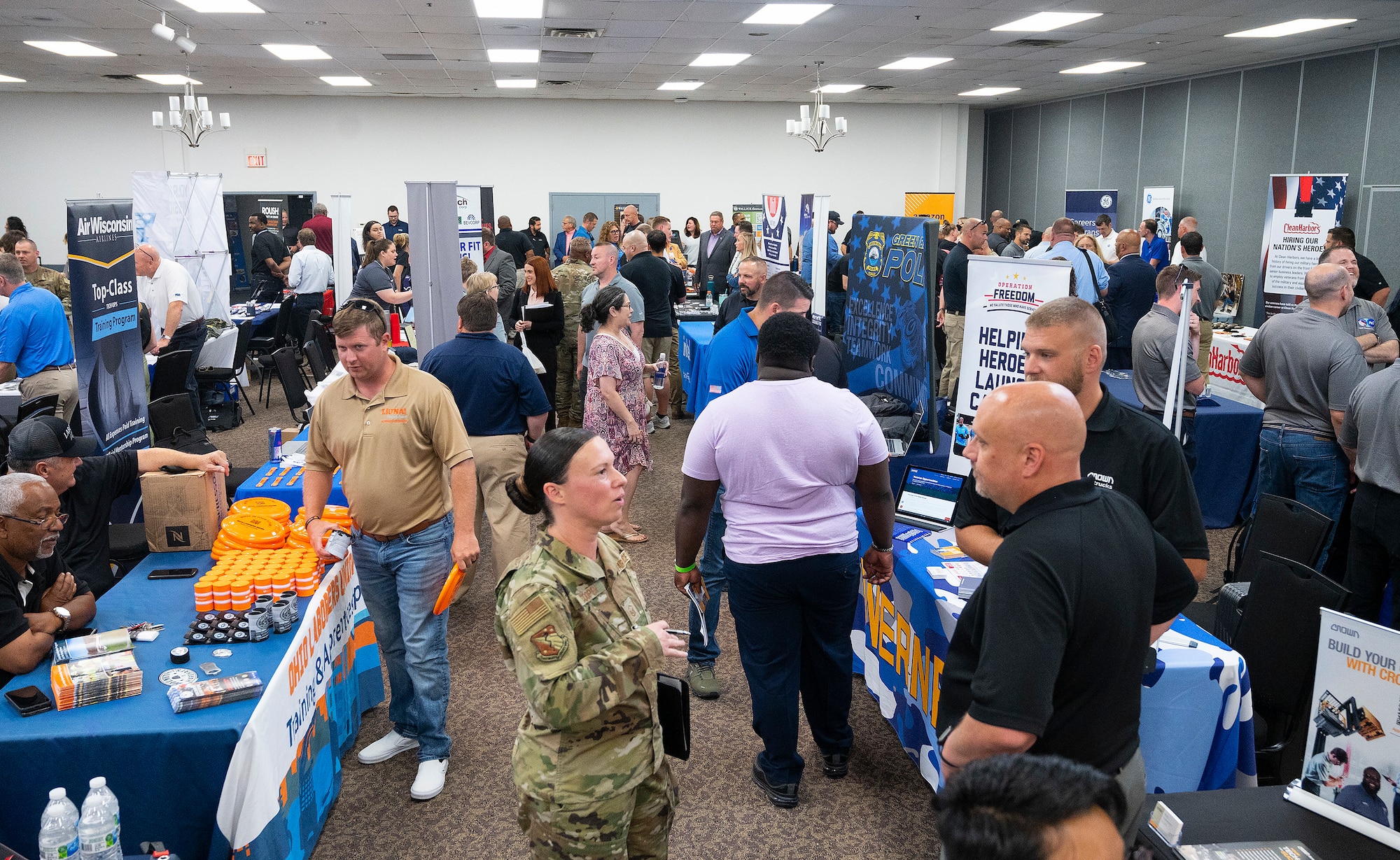 Master Sgt. Angie Cooper (center), U.S. Air Force School of Aerospace Medicine, talks with representatives of Crown Lift Truck, in a room crowded with company reps and job hunters at the Hire Our Heroes event June 22, 2022, at the Hope Hotel, Wright-Patterson Air Force Base, Ohio. More than 50 companies, with more than 50 thousand job openings, who set up tables to talk with active-duty Airmen, recent retirees and spouses. (U.S. Air Force photo by R.J. Oriez)