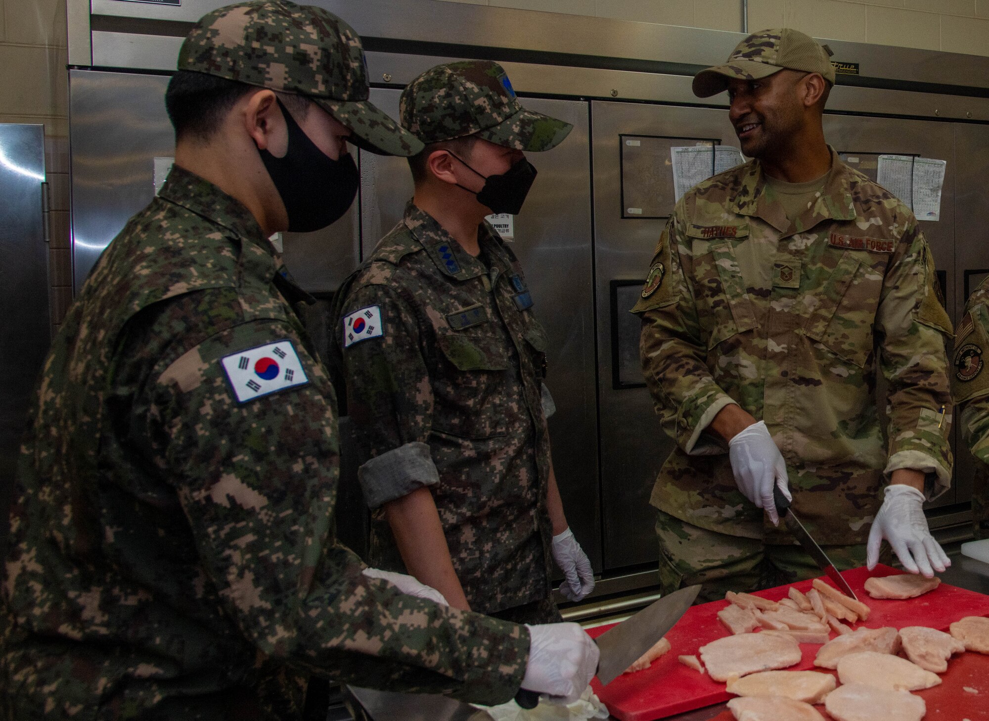 U.S. Service member cutting raw chicken in front of ROKAF service members