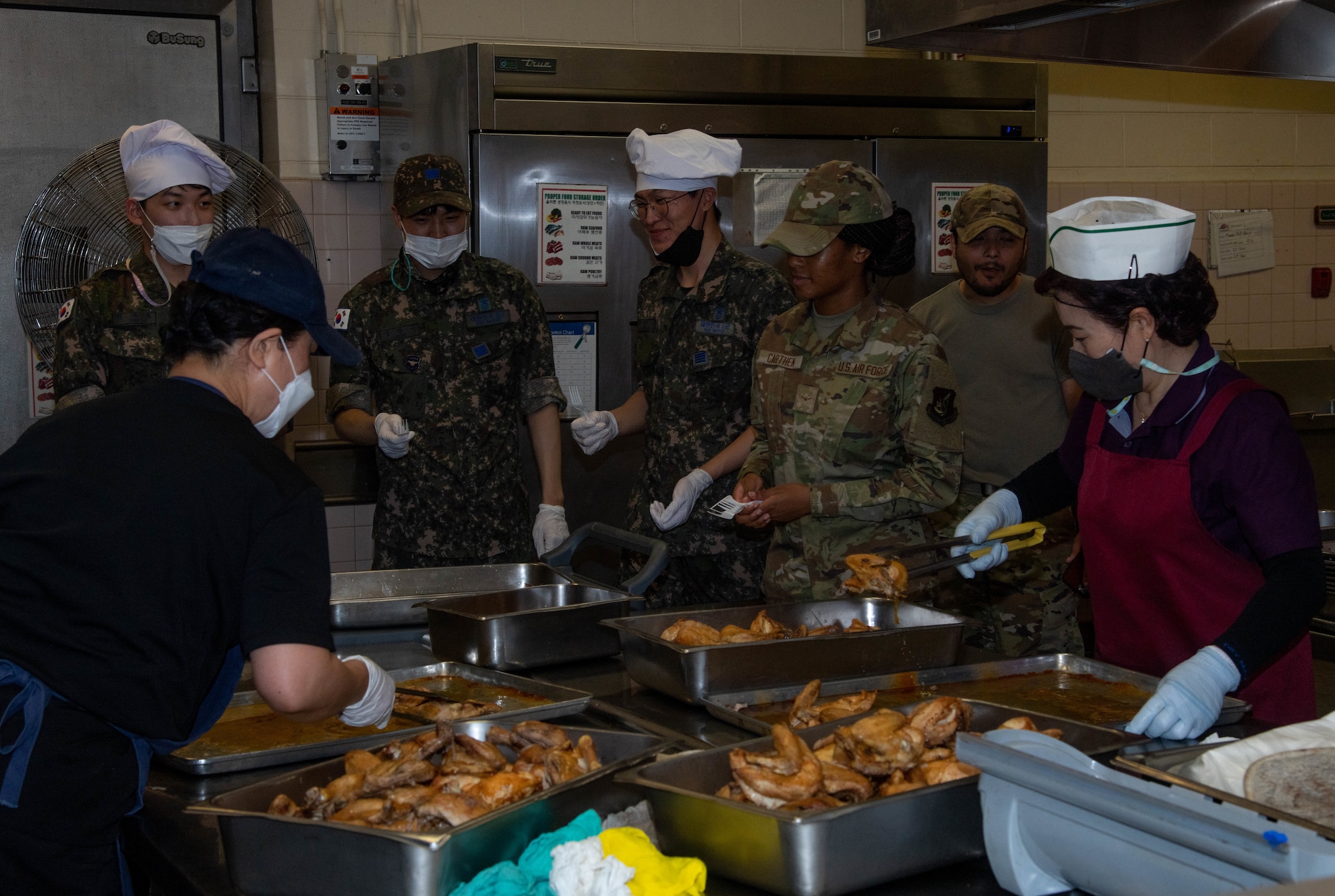 Service members in an industrial kitchen tasting roasted chicken