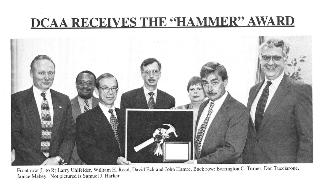 black and white photo of 7 individuals in business suits holding an award